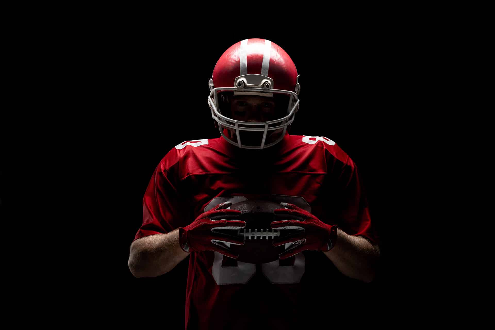 American football player standing with rugby helmet and ball against black background. Strong American Football Player concept for Championship Football Tournament
